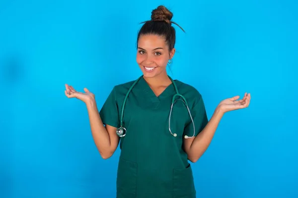 陽気な陽気な陽気な美しいですヒスパニック医師女性身に着けています緑医療制服上の青の背景保持二本のヤシコピースペース — ストック写真