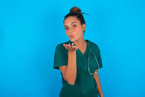 青い背景の上に制服を着た美人医師の女がカメラを見ながら手でキスを吹いてるのが可愛くてセクシー 愛の表現 — ストック写真