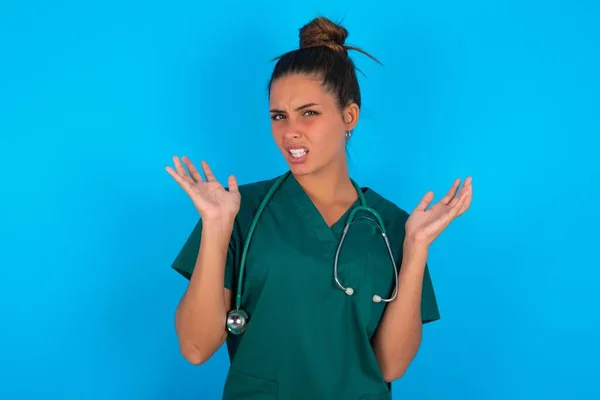 Oburzony Piękny Lekarz Hiszpański Kobieta Zielonym Mundurze Medycznym Nad Niebieskim — Zdjęcie stockowe