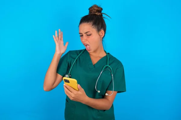 Злая Красивая Латиноамериканка Зеленой Медицинской Форме Синем Фоне Кричала Телефону — стоковое фото