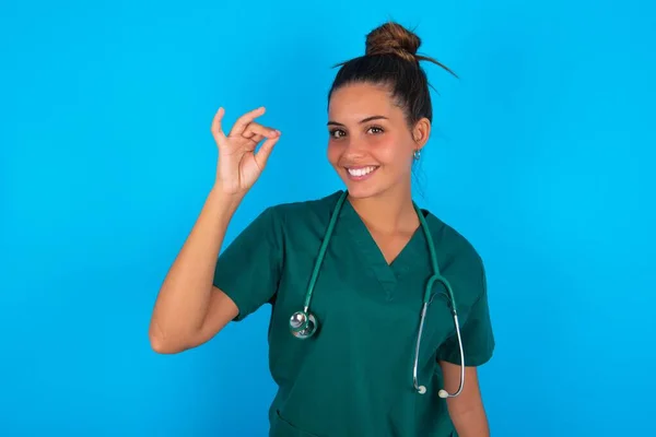 青い背景に緑色の制服を着た美しいヒスパニック系の医師女性が手で指摘し 7本の指のジェスチャーを中国語の看板言語で表示Q — ストック写真