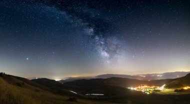 Santo Stefano di Sessanio, Abruzzo ve Rocca Calascio, İtalya üzerinde panoramik gece gökyüzü. Samanyolu galaksisi ve yıldızları aydınlatılmış köy üzerinde eşsiz tepeler üzerinde. Jüpiter gezegeni görünür.