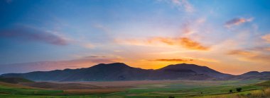 İtalya 'nın Castelluccio di Norcia dağlarında güzel bir günbatımı gökyüzü. Çiçekli tarlalar, Apeninler 'deki ünlü renkli çiçek düzlükleri. Mercimek ekinleri tarımı.