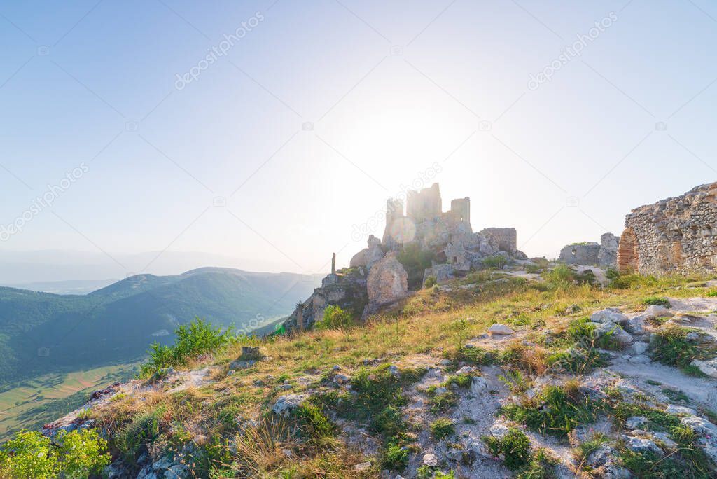 Castle ruins on mountain top at Rocca Calascio, italian travel destination, landmark in the Gran Sasso National Park, Abruzzo, Italy. Clear blue sky sun burst in backlight