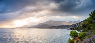 Kışın Rocky kıyı şeridi ve su körfezi, Riviera dei Fiori, Liguria, İtalya. Arka planda Menton kasabası var. Gün batımında dramatik gökyüzü.