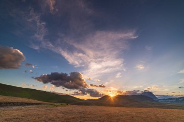 Kayalık dağlar, dağlık araziler ve otlaklar üzerinde gün batımı manzarası. Campo Imperatore, Gran Sasso, Apennines, İtalya. Dramatik dağ sırtında gökyüzünde renkli bulutlar.