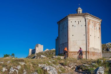 Rocca Calascio 'daki dağların tepesindeki MTB' ye giden adam ve kadın İtalya 'nın Gran Sasso Ulusal Parkı, Abruzzo, İtalya. Açık mavi gökyüzü