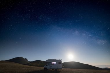 Campo Imperatore dağları üzerinde panoramik gece gökyüzü, Abruzzo, İtalya. Samanyolu galaksisi kavisi ve aydınlatılmış karavanın üzerindeki yıldızlar. Eşsiz tepelerde kamp yapma özgürlüğü.