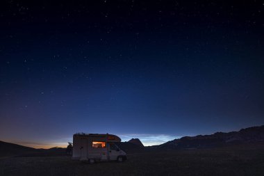 Campo Imperatore dağları üzerinde panoramik gece gökyüzü, Abruzzo, İtalya. Samanyolu galaksisi kavisi ve aydınlatılmış karavanın üzerindeki yıldızlar. Eşsiz tepelerde kamp yapma özgürlüğü.