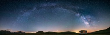 Campo Imperatore dağları üzerinde panoramik gece gökyüzü, Abruzzo, İtalya. Samanyolu galaksisi kavisi ve aydınlatılmış karavanın üzerindeki yıldızlar. Eşsiz tepelerde kamp yapma özgürlüğü.