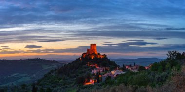 Rocca d 'Orcia, İtalya' nın Toskana şehrinde bir ortaçağ köyü ve kalesi. Alacakaranlıkta eşsiz bir manzara, taş kule dramatik gökyüzüne karşı kayalıklarda tünemişti..