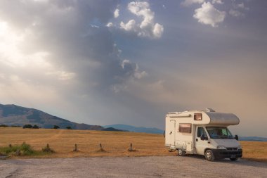 Yol kenarında güzel manzaralı bir karavan. Gün batımında dramatik bir gökyüzü, İtalya 'da eşsiz dağlık arazi ve tepenin üzerindeki manzaralı bulutlar, alternatif vanlife tatil konsepti.