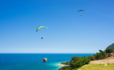 Portonovo, Italy - May 8, 2022: Paragliders flying over scenic coast line of the Conero natural, Italy. Extreme sport over dramatic coast headland in the mediterranean sea tourism destination