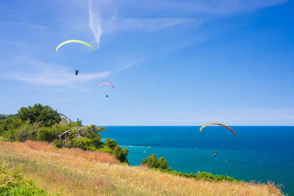 Paragliderler Conero 'nun doğal kıyı şeridi üzerinde uçuyorlar, İtalya. Akdeniz turizm beldesinde dramatik sahil burnu üzerinde aşırı spor