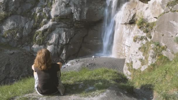 スローモーション 女性は山の上の滝を見て 風光明媚な高山の風景の中に屋外活動を行う一人 アルプスの夏休み フィットネスの幸福の自由 — ストック動画