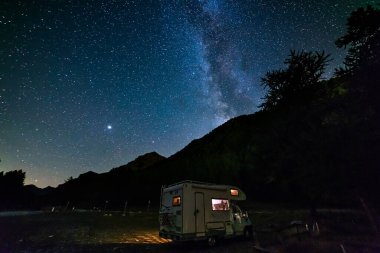 Karavan Alplerde panoramik gece gökyüzü altında. Samanyolu galaksisi ve yıldızları aydınlanmış karavanın üzerinde. Eşsiz bir arazide kamp yapma özgürlüğü..