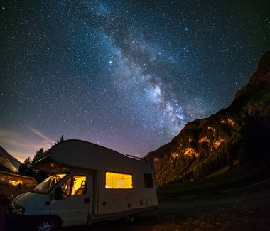 Karavan Alplerde panoramik gece gökyüzü altında. Samanyolu galaksisi ve yıldızları aydınlanmış karavanın üzerinde. Eşsiz bir arazide kamp yapma özgürlüğü..