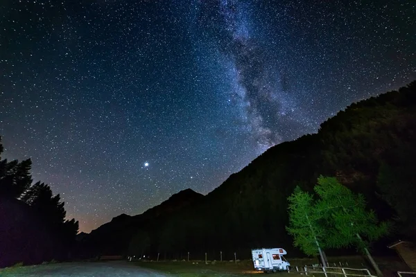 Karavan Alplerde panoramik gece gökyüzü altında. Samanyolu galaksisi ve yıldızları aydınlanmış karavanın üzerinde. Eşsiz bir arazide kamp yapma özgürlüğü..