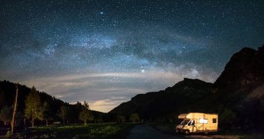 Karavan Alplerde panoramik gece gökyüzü altında. Samanyolu galaksisi ve yıldızları aydınlanmış karavanın üzerinde. Eşsiz bir arazide kamp yapma özgürlüğü..
