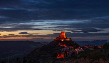 Rocca d 'Orcia, İtalya' nın Toskana şehrinde bir ortaçağ köyü ve kalesi. Alacakaranlıkta eşsiz bir manzara, taş kule dramatik gökyüzüne karşı kayalıklarda tünemişti..