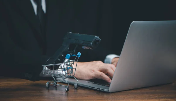 Çevrimiçi satıcı dükkanından silah almak, internet sitesinden ya da sosyal medyadan tabanca almak için bilgisayar klavyesine yazı yazan iş adamlarının elleri, tabancalı alışveriş arabası.