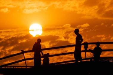Silhouettes of construction workers on the background of the sunset sky with a huge disk of the sun. High quality photo