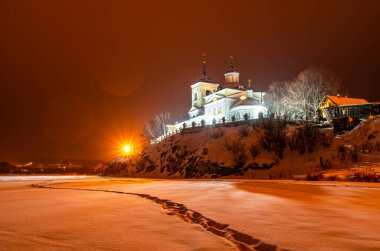 illuminated russian orthodox church on a cliff of a snow-covered frozen river on a winter night. High quality photo