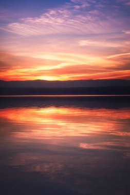 Beautiful colorful sunset sky and forest on the horizon reflecting in the water of the lake. High quality photo