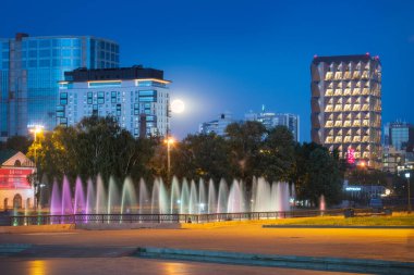 Full moon in the night sky over modern buildings and colored illuminated fountains in the center of yekaterinburg city. High quality photo