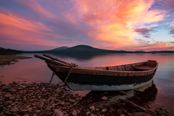 Boat moored by the lake, under a magnificent sunset sky with orange and pink clouds. High quality photo