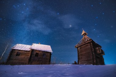 Old abandoned wooden chapel and building under winter night sky full of stars and Ursa Major constellation and Milky Way