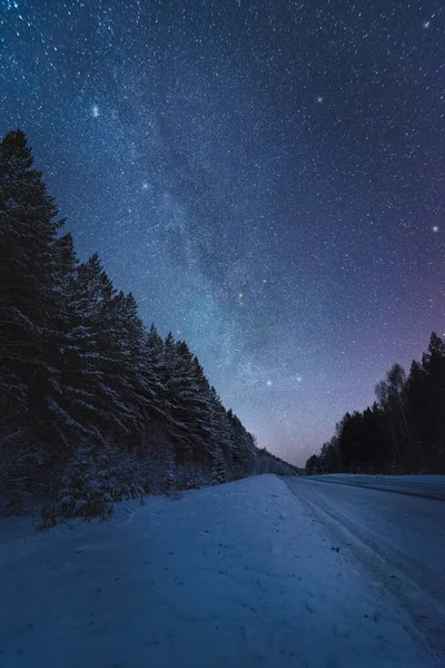 Winter road in the forest under beautiful night sky with Milky Way and lot of stars — стоковое фото