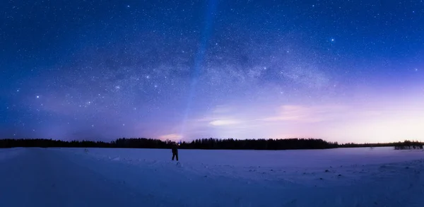 Milky Way Arc and sky full of stars above the snow field and a man with flashlight pointing in the sky — стоковое фото