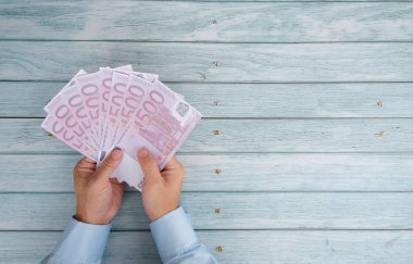 Ahşap bir arka planda kağıt para tutan kadın elleri.