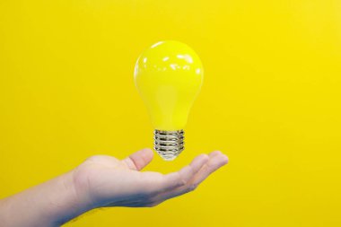hand holding yellow light bulb on a bright background