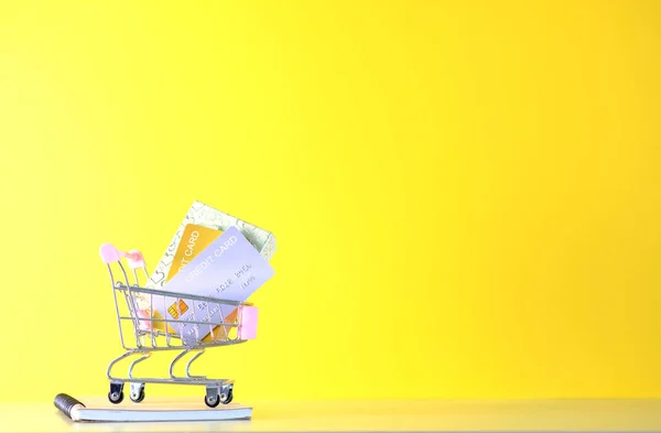 黄色の背景にお金とクレジットカードでショッピングカート — ストック写真