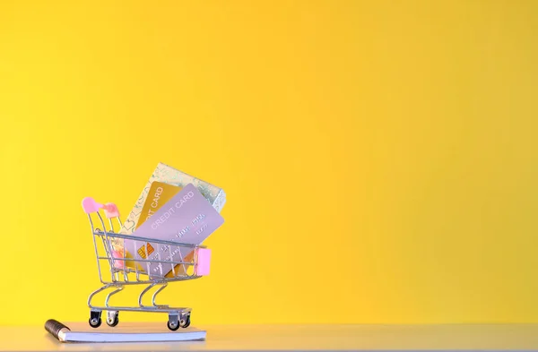 Sarı Arka Planda Para Kredi Kartı Olan Alışveriş Arabası — Stok fotoğraf