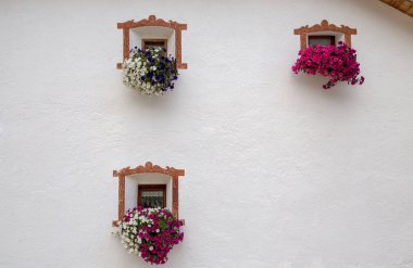 Three small windows decorated with flowers with a white facade