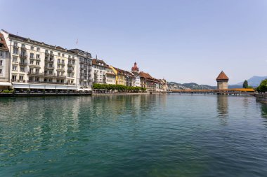 LUCERNE, SWitzERLAND, 21 Haziran 2022 - İsviçre 'nin başkenti Lucerne' deki Reuss nehrinin arka planındaki eski binalar ve yün kaplı Kapellbrucke Köprüsü manzarası