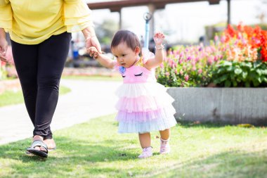Anne bahçede yürümek için kızının elini tutuyor.
