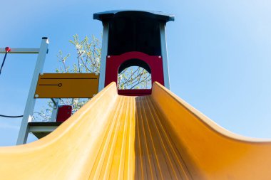 Parlak renkli sarı oyun seti. Oyun oynayan çocuklar için bir oyun parkında kaydırma ve tırmanma çerçevesi var.