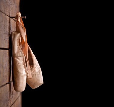 Used ballet shoes hanging on wooden background clipart