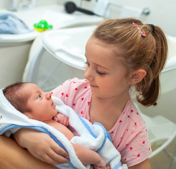 新生児の男の子の最初の風呂 赤ん坊は妹の腕の中のバスローブにいる — ストック写真