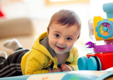 Birkaç aylık bebek, oyuncaklarıyla birlikte yumuşak bir halıda gülümsüyor..
