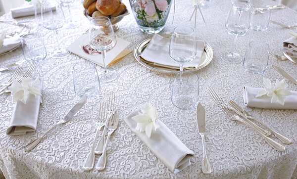 Bridal mise en place with white lace tablecloth and silver cutlery.