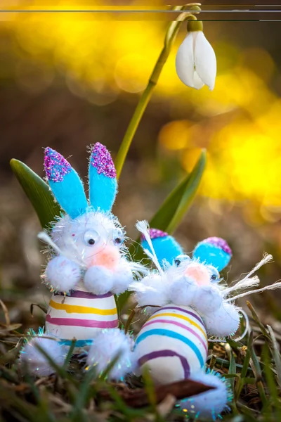 Toy easter bunnies lounging in the grass under a white snowdrop — Stock Photo, Image