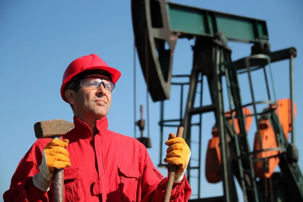 Oil Industry Worker Holding Sledgehammer Next to Pump Jack. — Stock Photo, Image