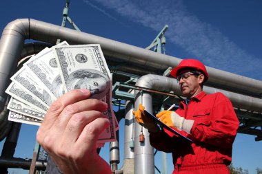 Petrol rafinerisinin içindeki petrol mühendisinin önünde Amerikan dolarları tutuyor.