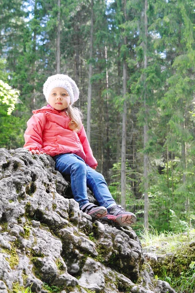 Liten flicka sitter på lilla berg i gröna skogen — Stockfoto