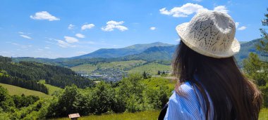 Hippi kadın sırtı kayaya dönük duruyor ve bir nehir ve vadisi olan güzel yeşil bir manzaraya bakıyor. Turist bir tepede duruyor ve manzaraya hayran. Yurtiçi turizm